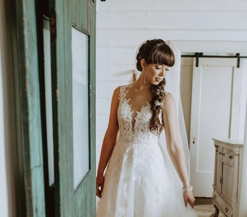 A bride in a lace and tulle gown beside a weathered green vintage door in a white shiplap room
