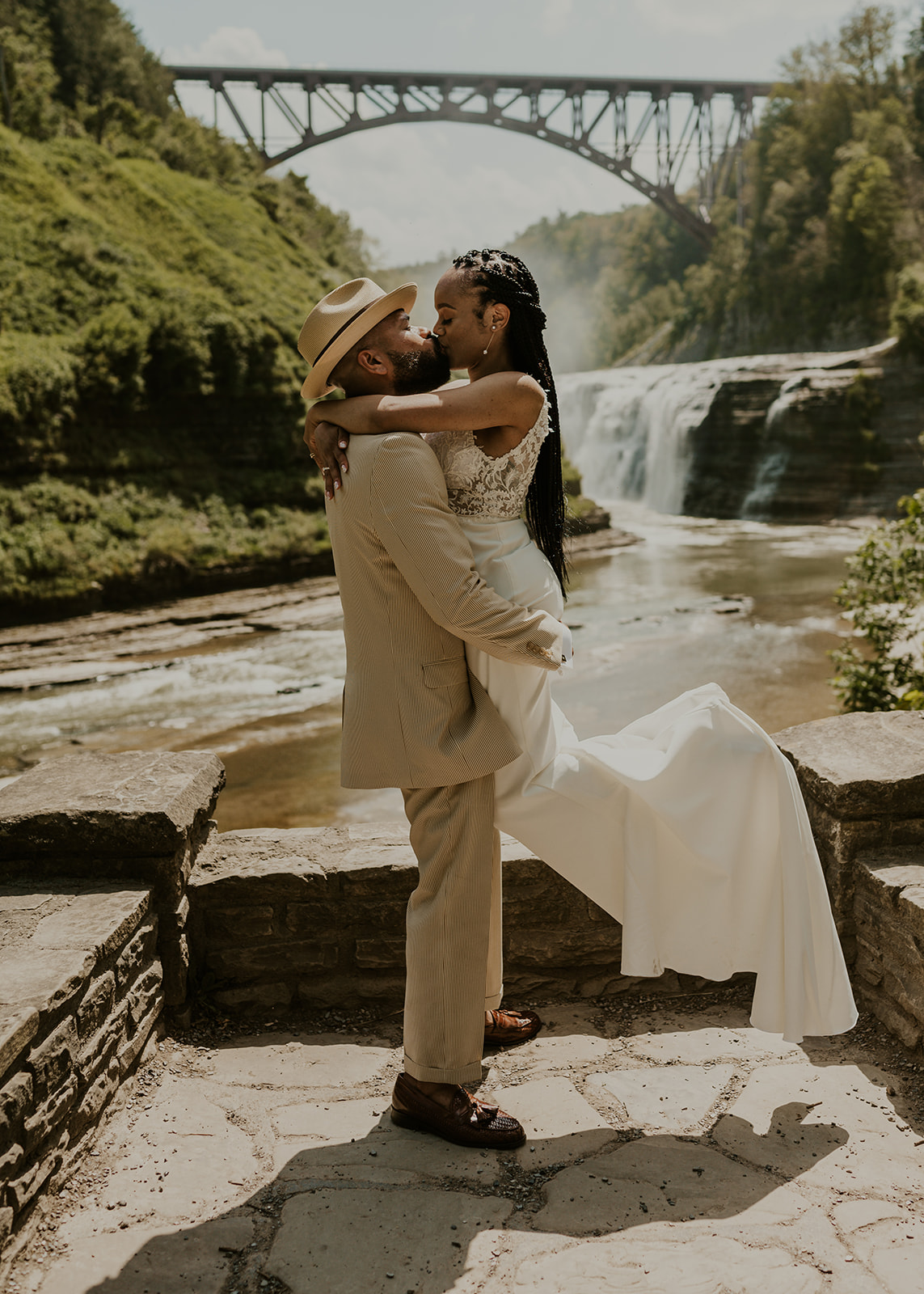 A couple kissing on the stone overlook wall at Letchworth, the Upper Falls and the arched railroad bridge over the gorge behind them