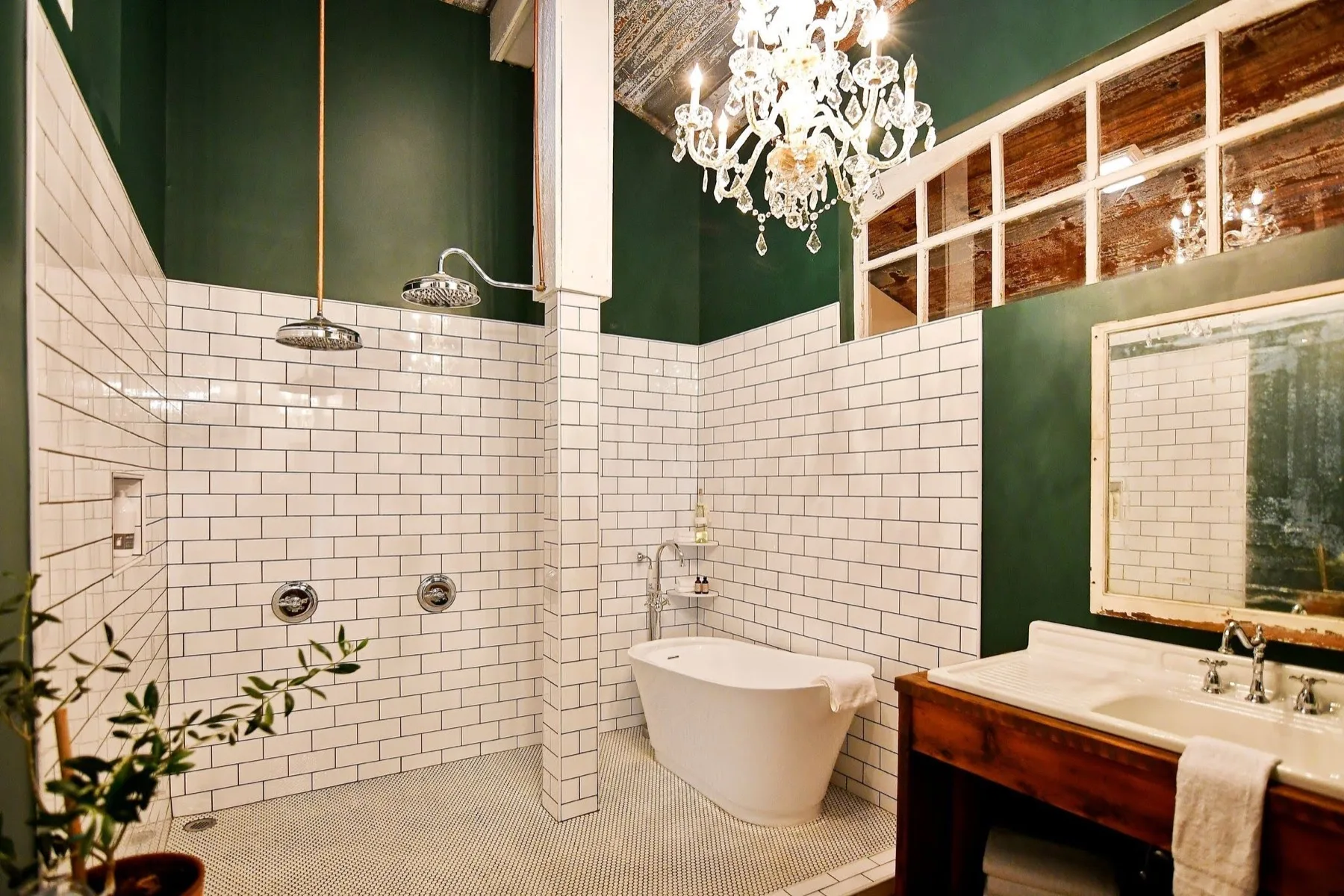 Emerald green bathroom with a crystal chandelier above a freestanding oval soaking tub and a subway tiled shower with two rain heads