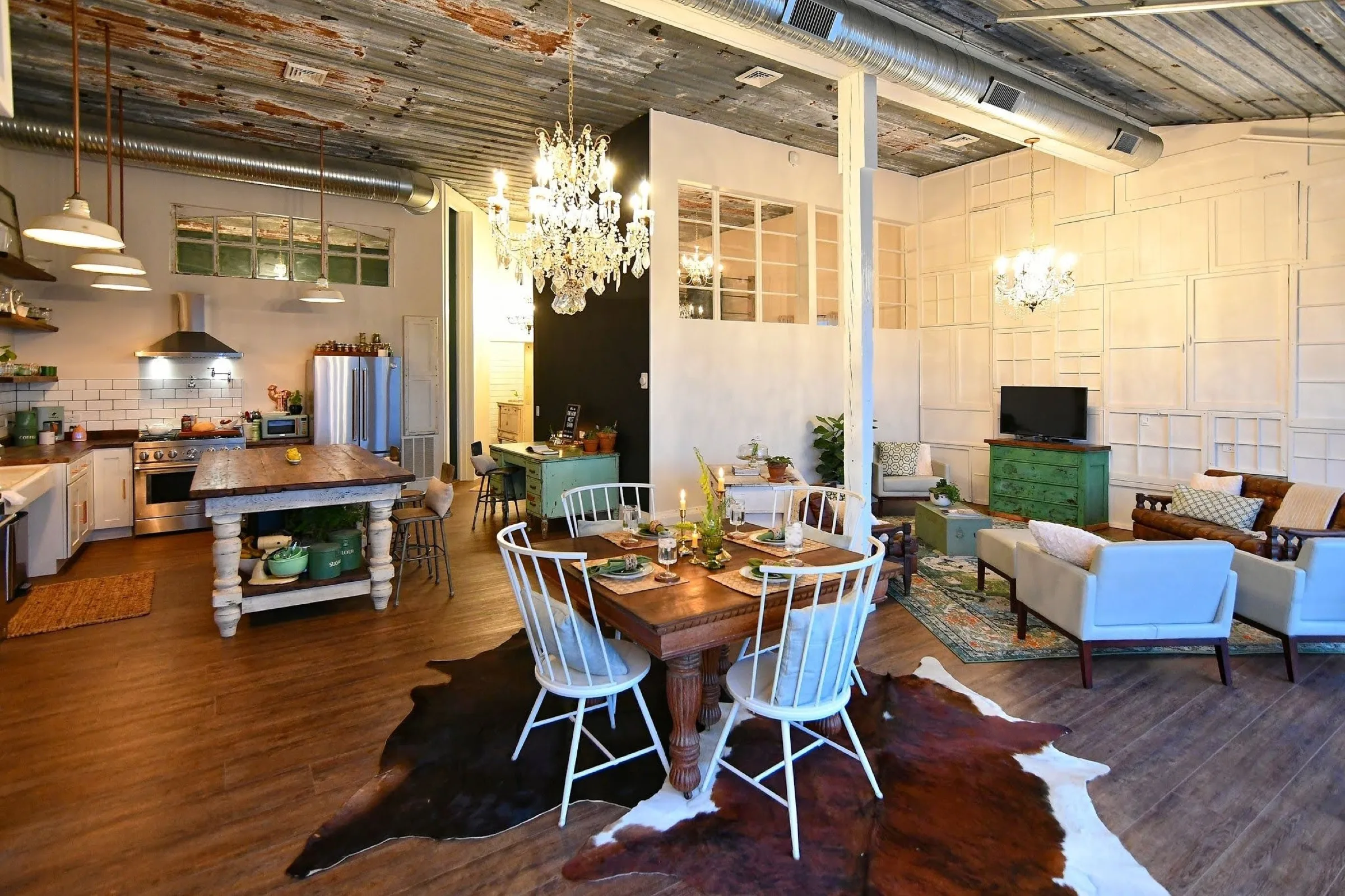 The Highbanks great room, farm table under two crystal chandeliers and a rusted tin ceiling