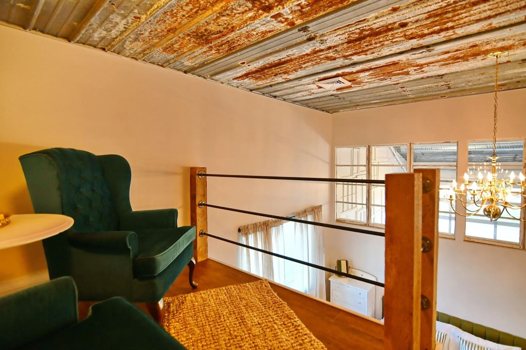 The loft nook above the living room, an emerald velvet wingback chair behind a cable and timber railing