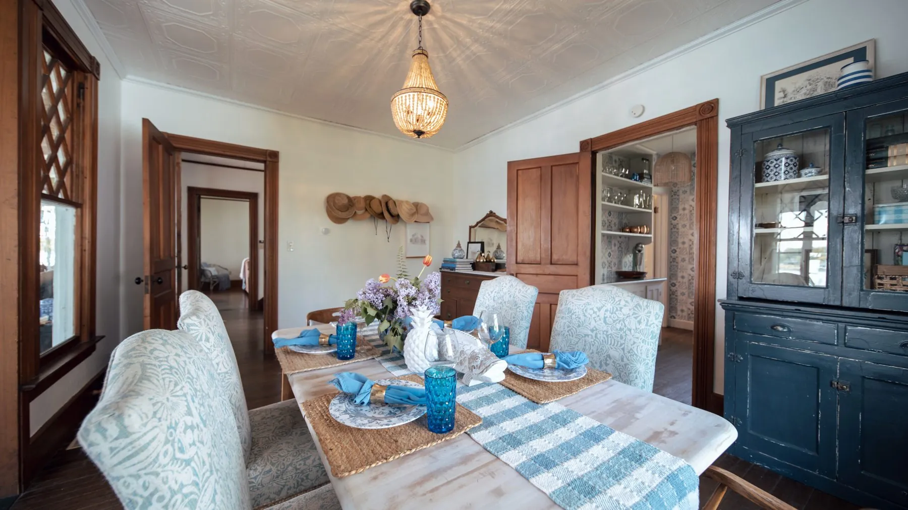 The lake house dining room, a whitewashed table set with blue and white china under a beaded chandelier and a pressed tin ceiling