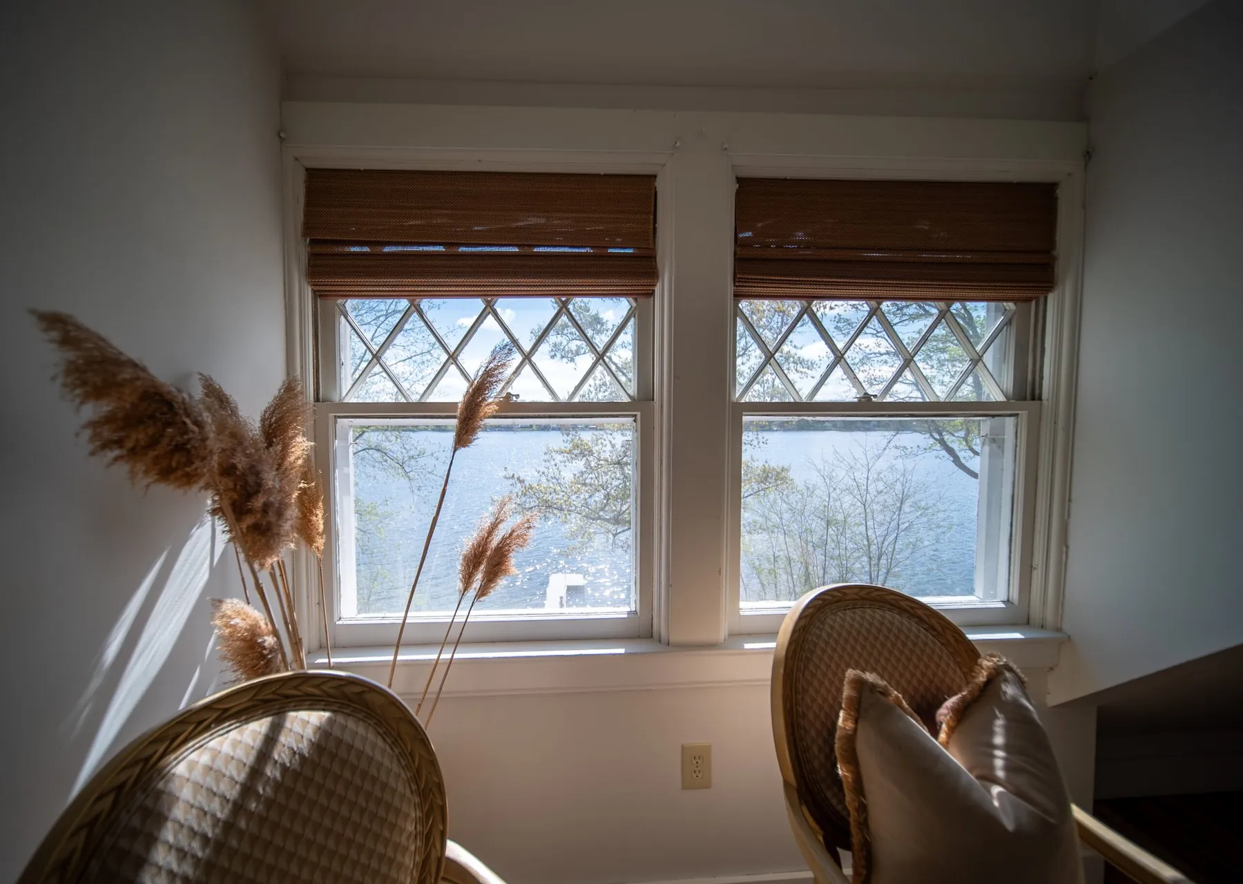Two diamond-leaded windows at the lake house looking straight out over Silver Lake, rattan chairs and dried pampas in front of them