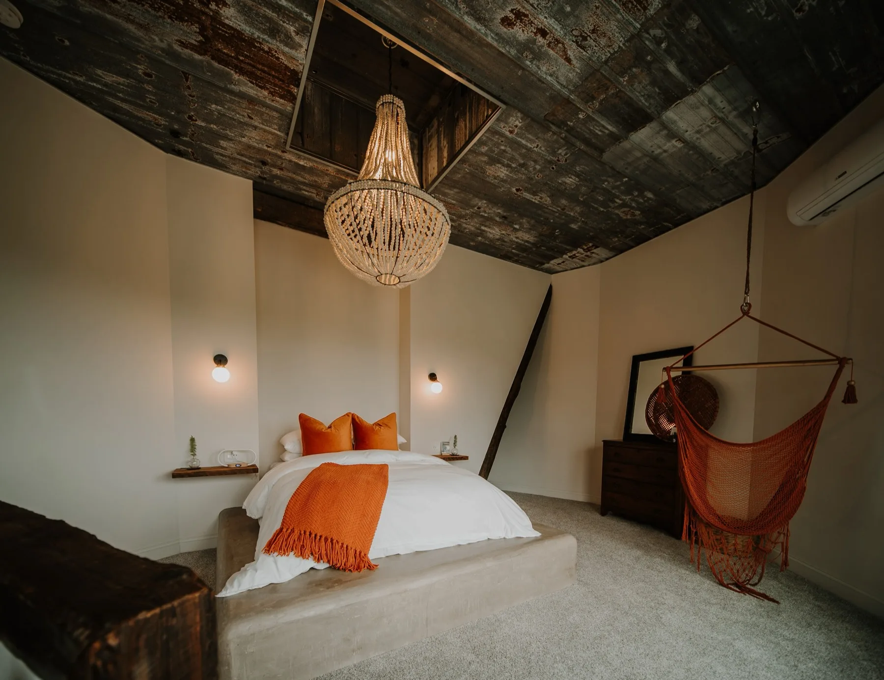 Third bedroom under a weathered corrugated ceiling, with a woven pendant and an orange rope hanging chair