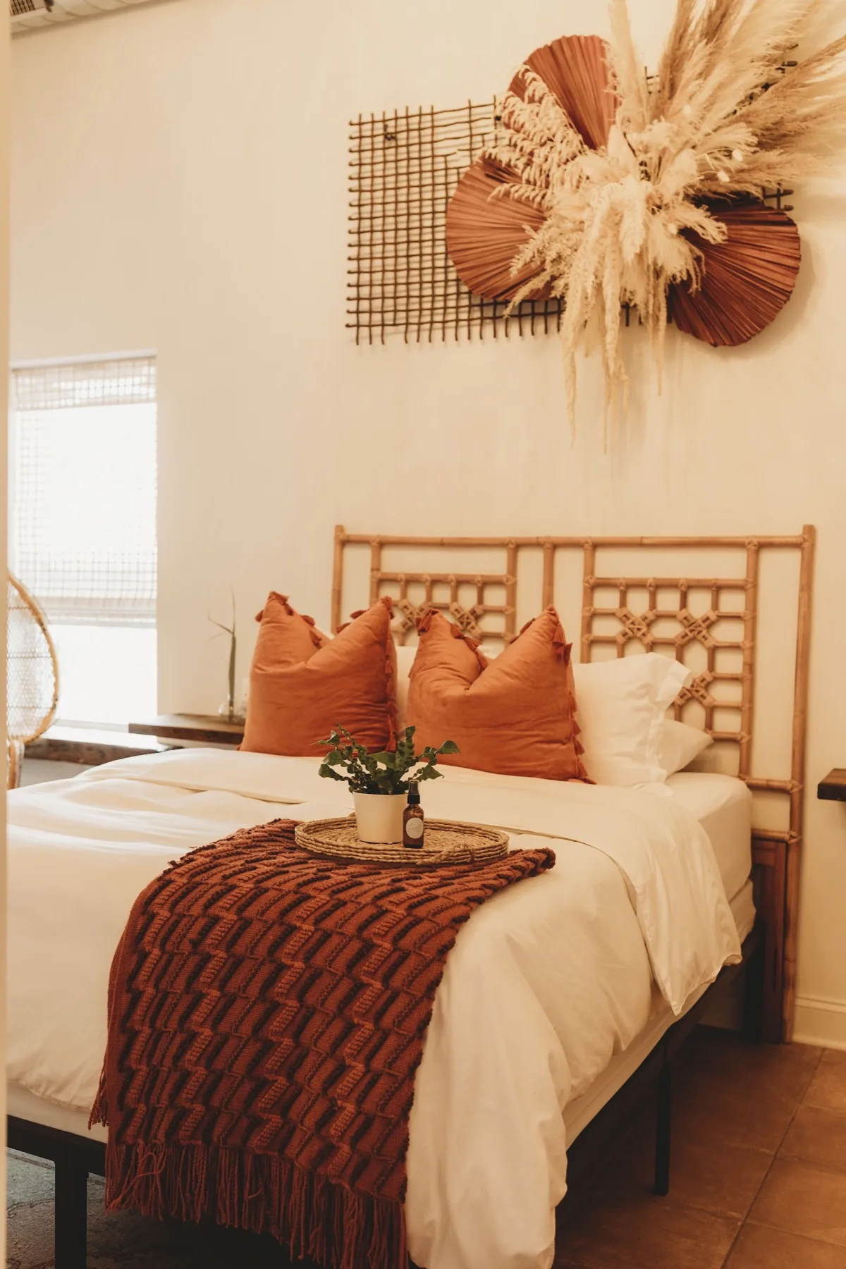 Bedroom with a rattan lattice headboard, rust orange pillows and dried pampas wall art