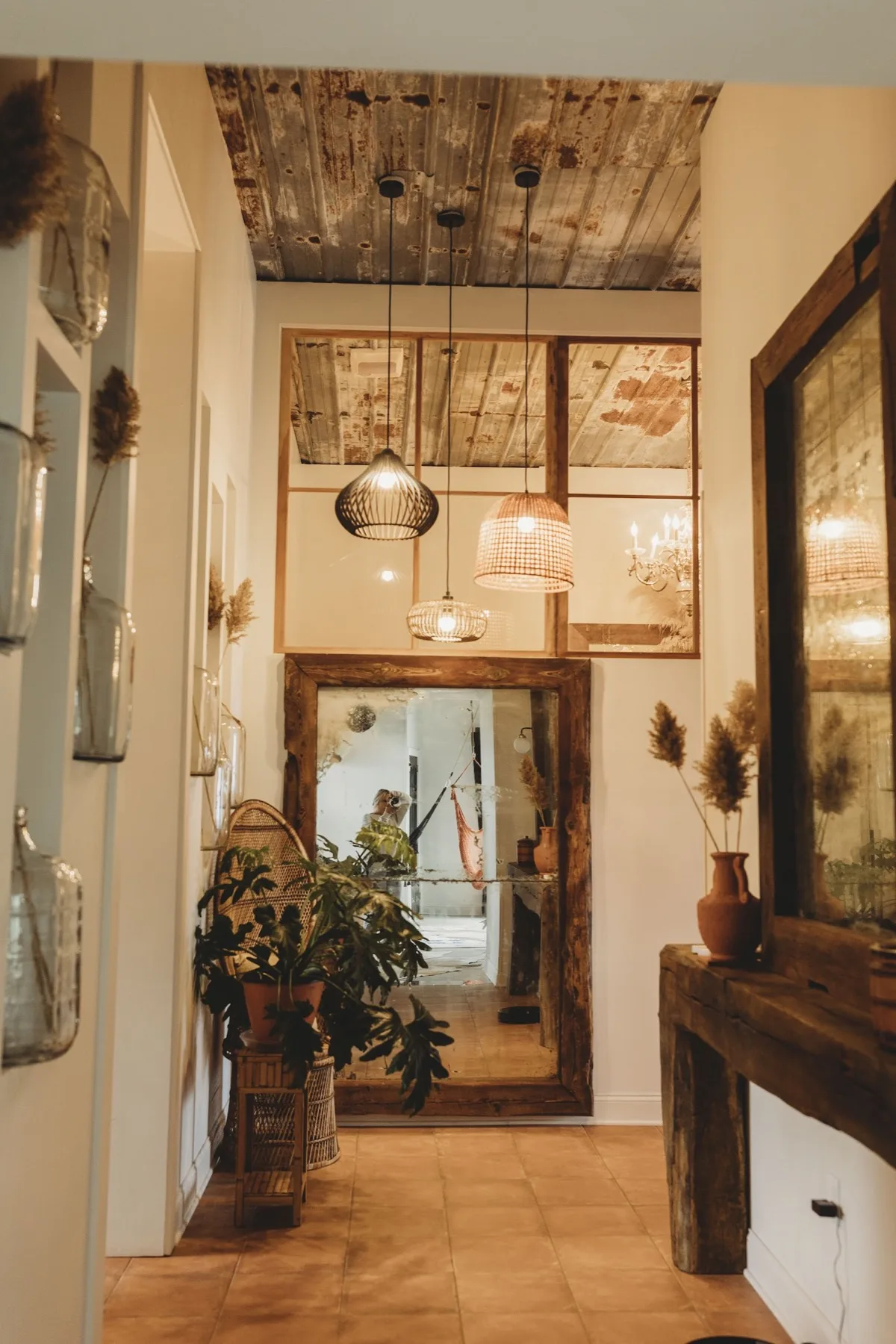 The entry hallway with an oversized vintage framed mirror, hanging pendants and dried pampas in bud vases on a terracotta floor