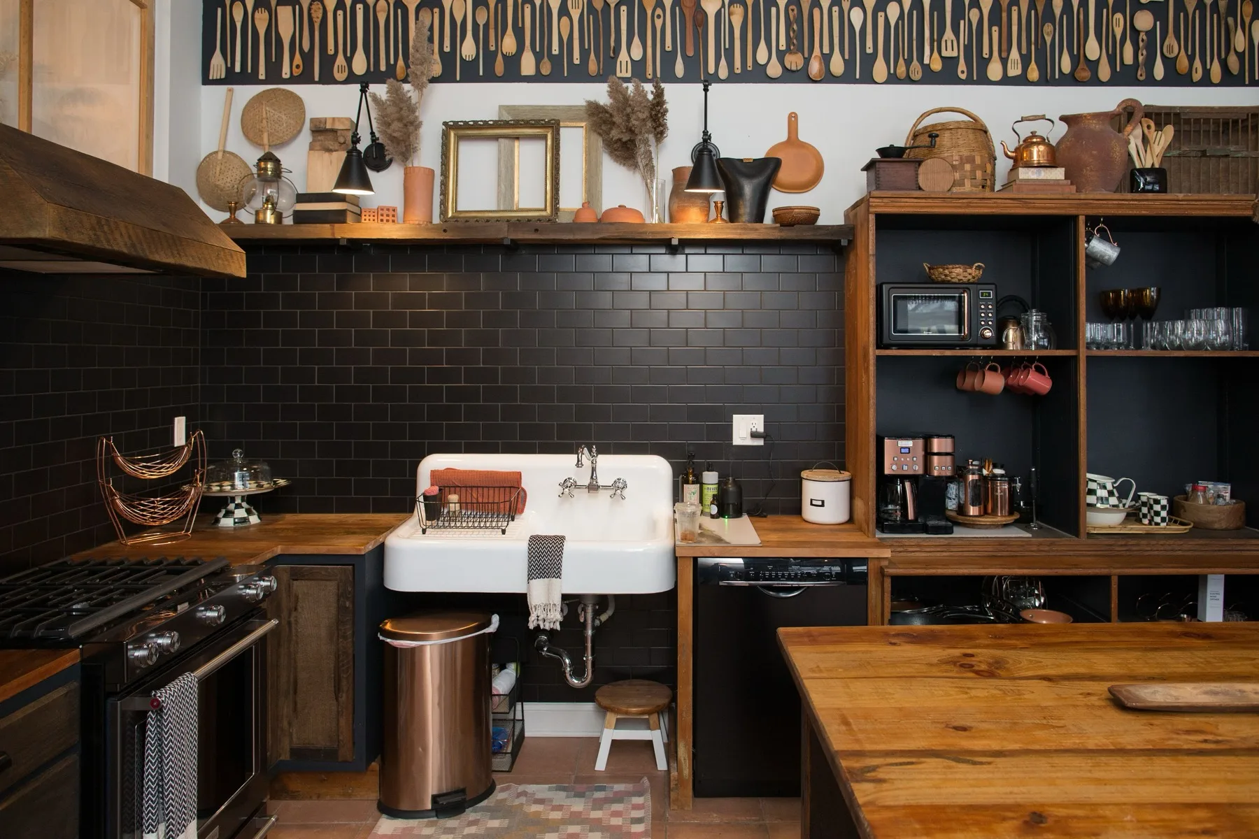 Kitchen with black subway tile, a farmhouse sink, copper accents and a wall display of vintage wooden spoons