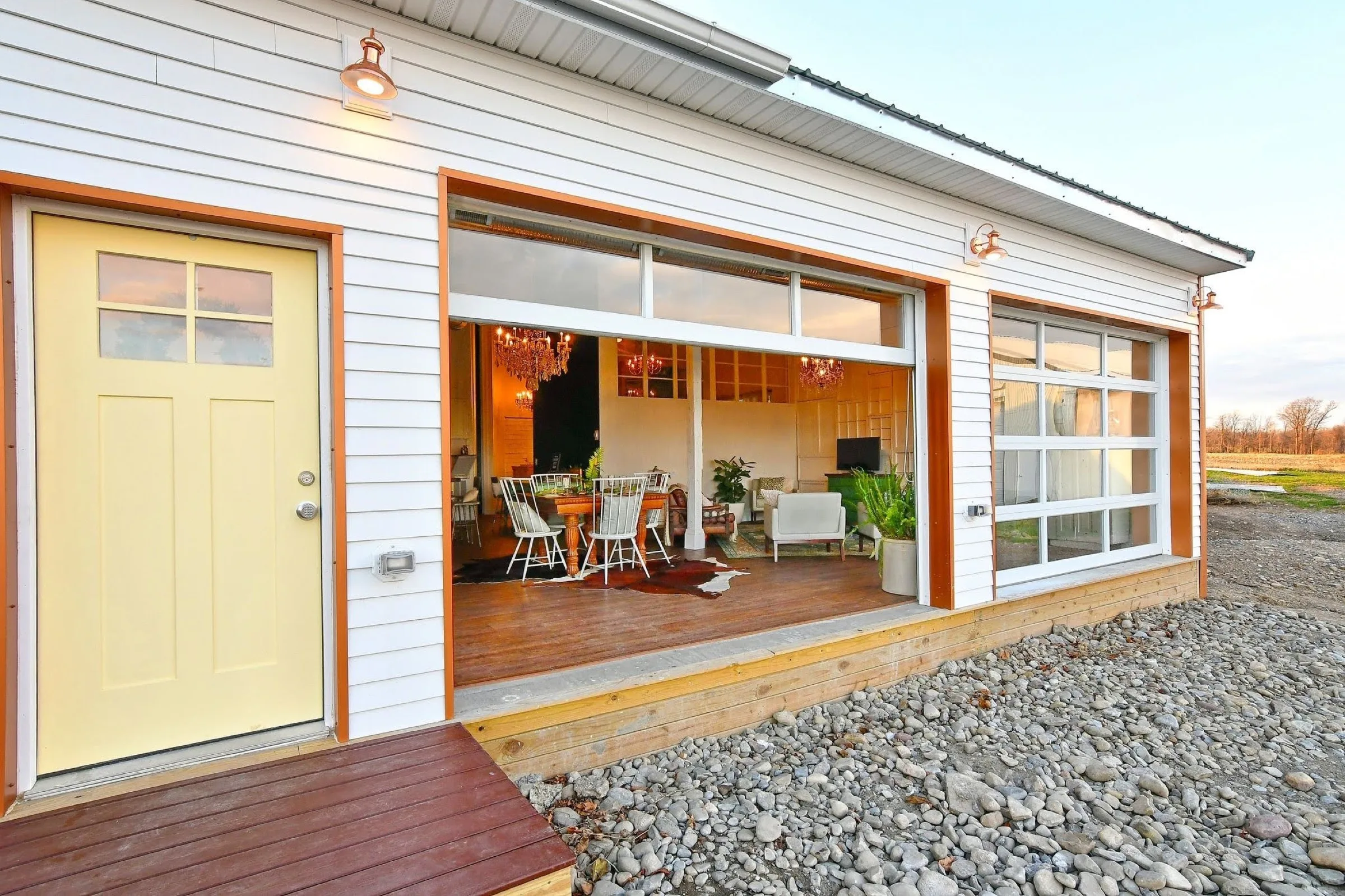 The West Barn at dusk, glass garage doors rolled open onto the field with the chandeliers lit inside