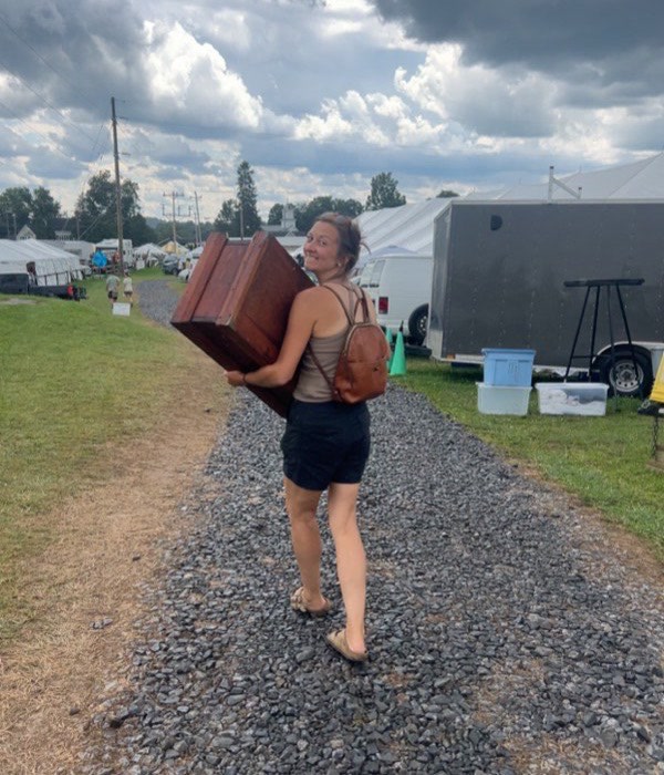 Amanda carrying a wooden antique down a gravel path at an outdoor market